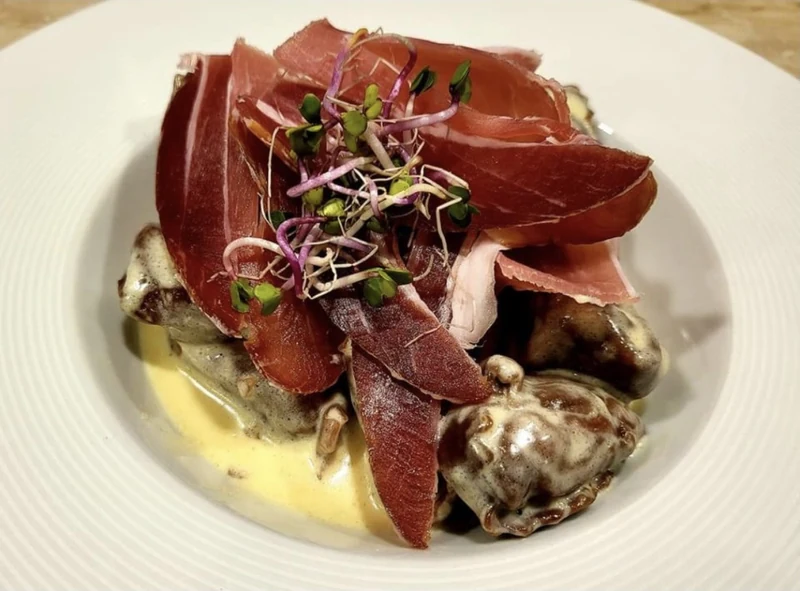 Assiette en sauce crémeuse, fines tranches de viande séchée et jeunes pousses.